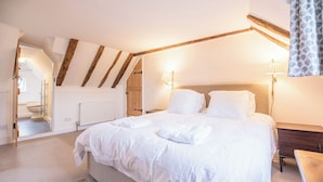 A bedroom with a large bed, wooden beams on the ceiling, a nightstand, and a lamp.