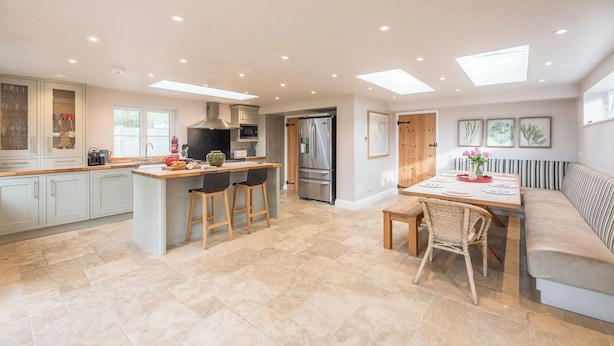 A modern kitchen with a central island, bar stools, a dining table with chairs, and a sofa.