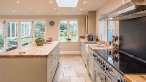 A modern kitchen with a large island, a built-in oven, and a view of the garden through the windows.