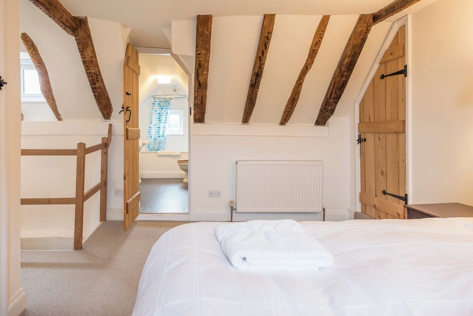 A bedroom with exposed wooden beams, a white radiator, and a bed with a white comforter.