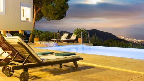 An infinity pool with lounge chairs and a view of a cityscape and mountains.