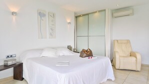 A hotel room with a bed, a bedside table with a lamp, a chair, and a window with blinds.