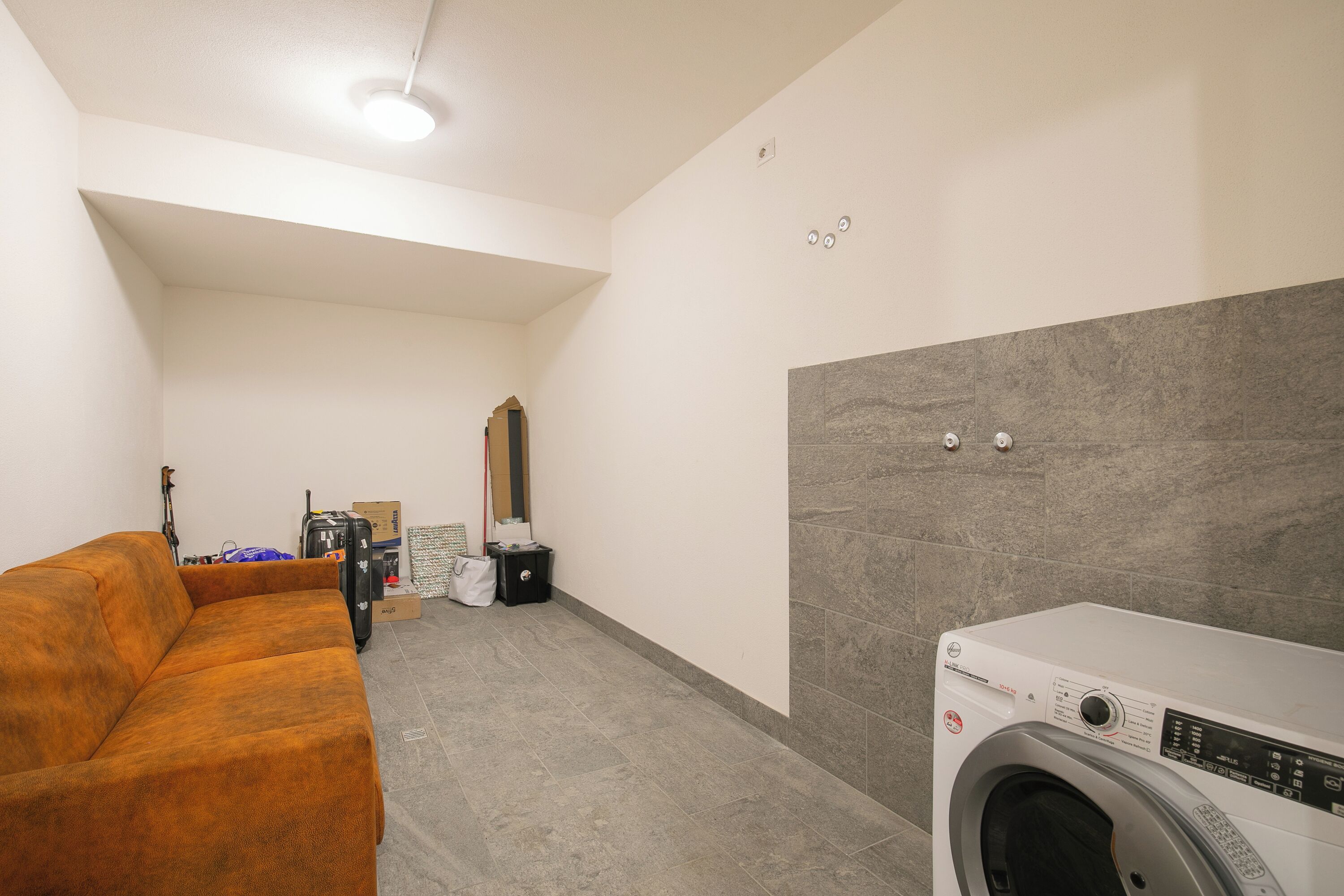 Een wasruimte met een wasmachine, een bank en een spiegel.