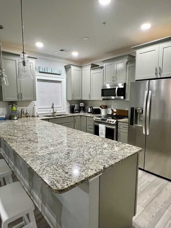 A modern kitchen with granite countertops, stainless steel appliances, and light gray cabinetry.