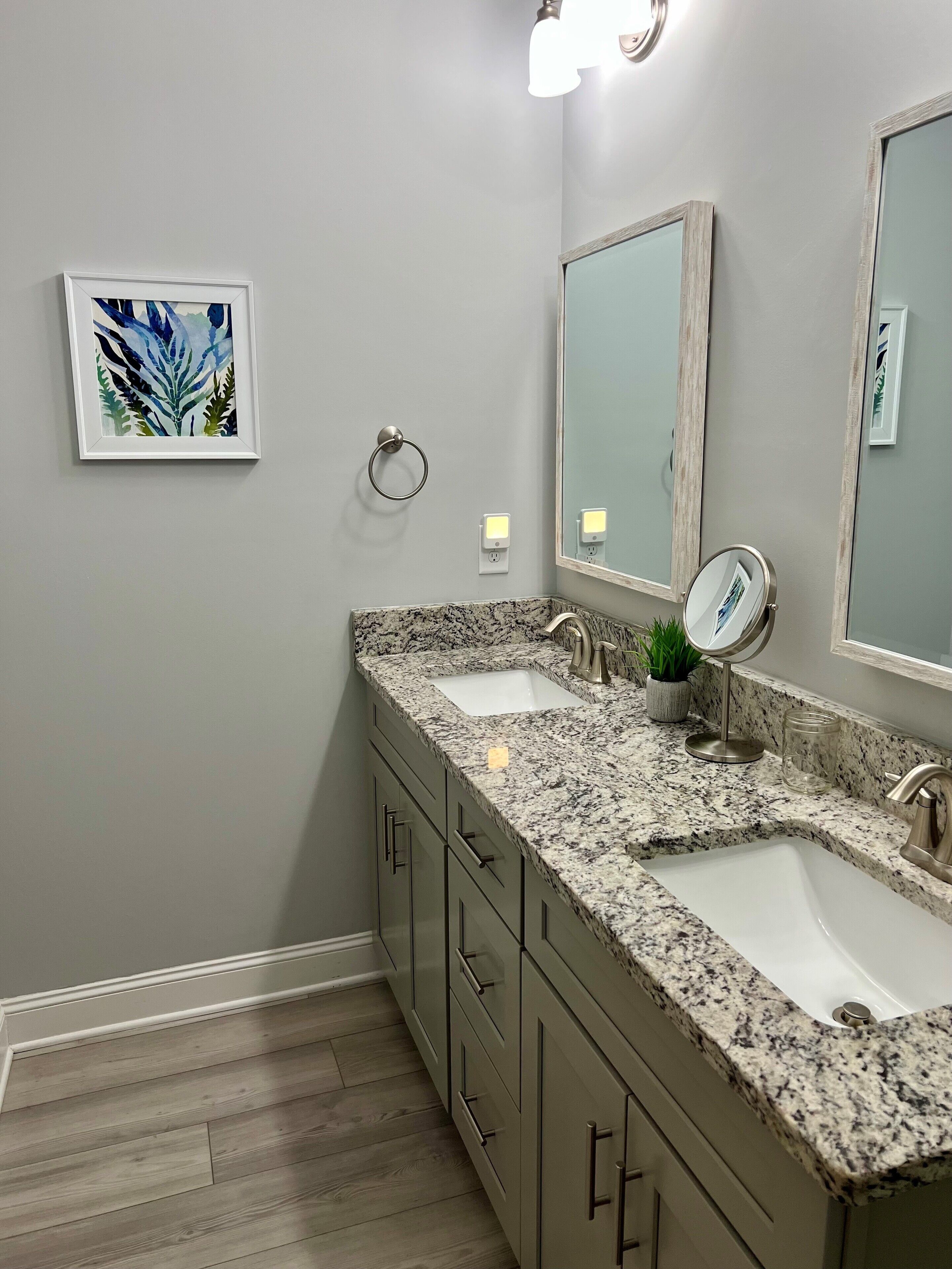 Une salle de bain avec deux lavabos, un miroir, un porte-serviettes et une œuvre d’art encadrée accrochée au mur.