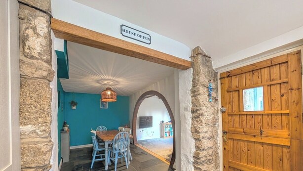 A dining area with a table and chairs, a stone wall, and a wooden door. - The Old Barn near St Ives - Rustic Charm & Space (Saint Ives)