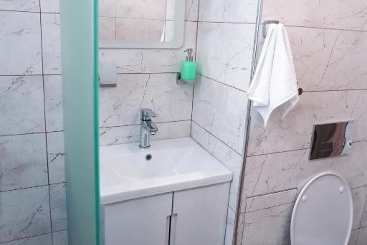 Une salle de bain avec un lavabo blanc, un miroir, un distributeur de savon vert et une serviette blanche accrochée au mur.
