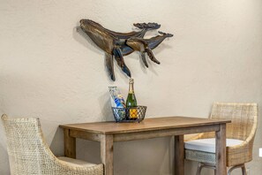 Una mesa de comedor con una escultura metálica encima, una cesta con una botella y sillas de mimbre.