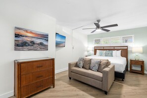 Un dormitorio con cama, ventilador de techo, cómoda, mesita de noche y televisor montado en la pared.