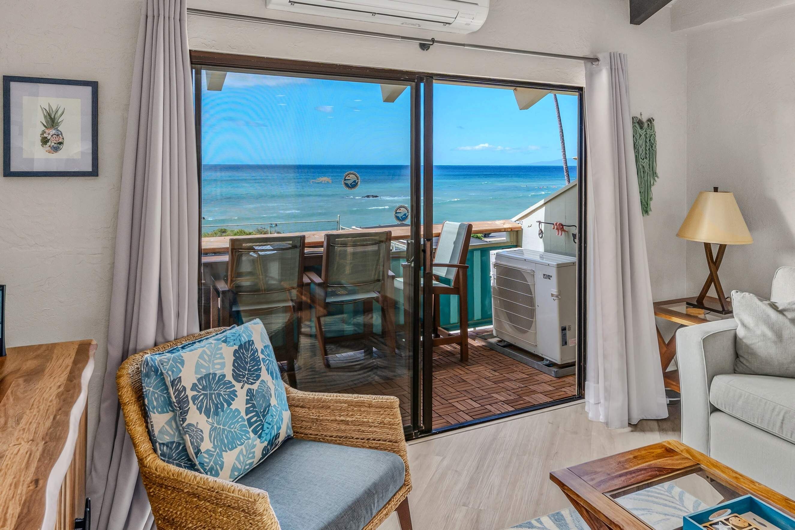 A room with a view of the ocean, a dining area with chairs and a table, and a seating area with a couch and a lamp.
