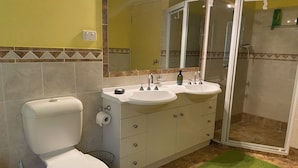 Une salle de bain comprenant des toilettes, deux lavabos, un miroir et un espace douche.
