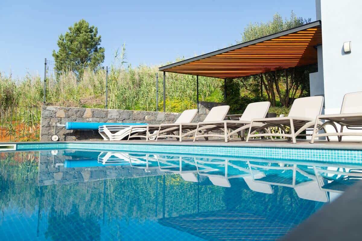 Una piscina con sillones de descanso, un muro de piedra y una pérgola de madera.