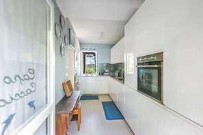 Una cocina moderna con armarios blancos, horno empotrado y ventana con vistas a zonas verdes.