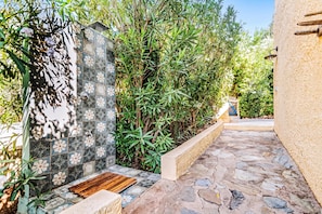 A stone pathway leading to a door with a tiled wall, surrounded by greenery.