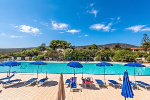 A swimming pool with blue umbrellas and sun loungers, surrounded by trees and hills. - Una Finestra Sul Mare Capocaccia, Alghero, Italy (Alghero)