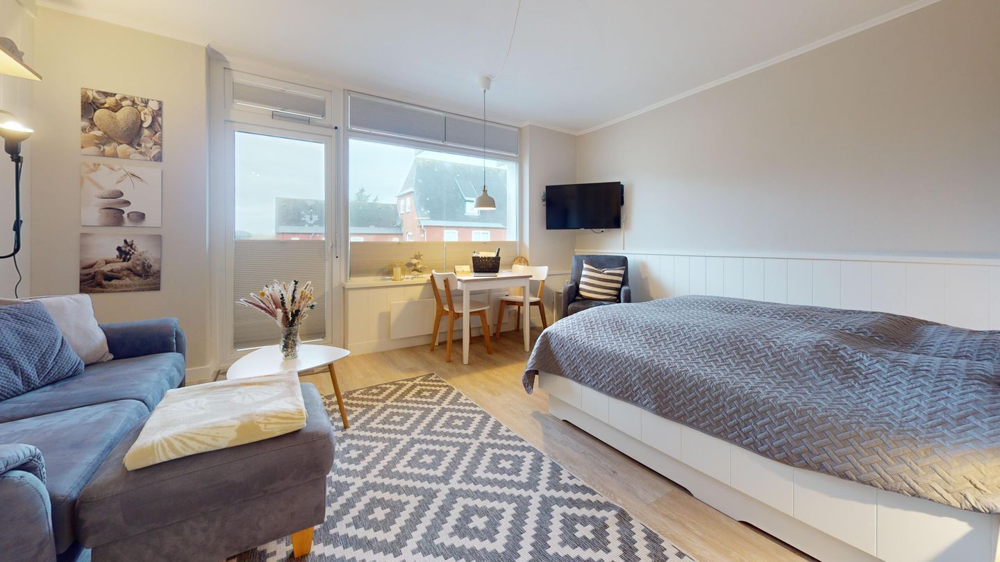 A modern bedroom with a bed, a sofa, a small table, and a TV.