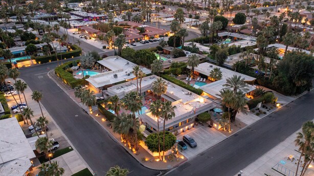 An aerial view of a hotel with multiple buildings, palm trees, and a parking lot.