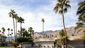 A building with a flat roof, palm trees, and mountains in the background.