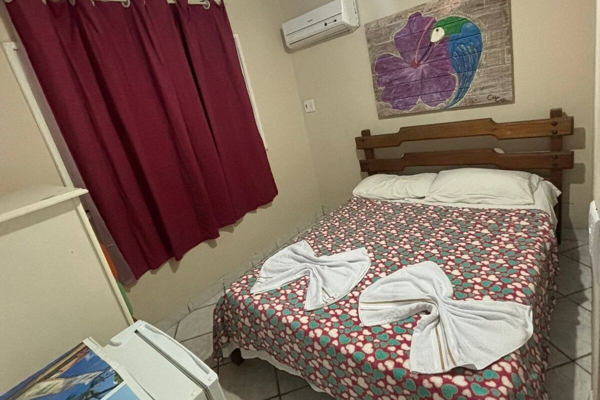 Une chambre à coucher avec un lit, des rideaux rouges, un climatiseur fixé au mur et un tableau coloré.
