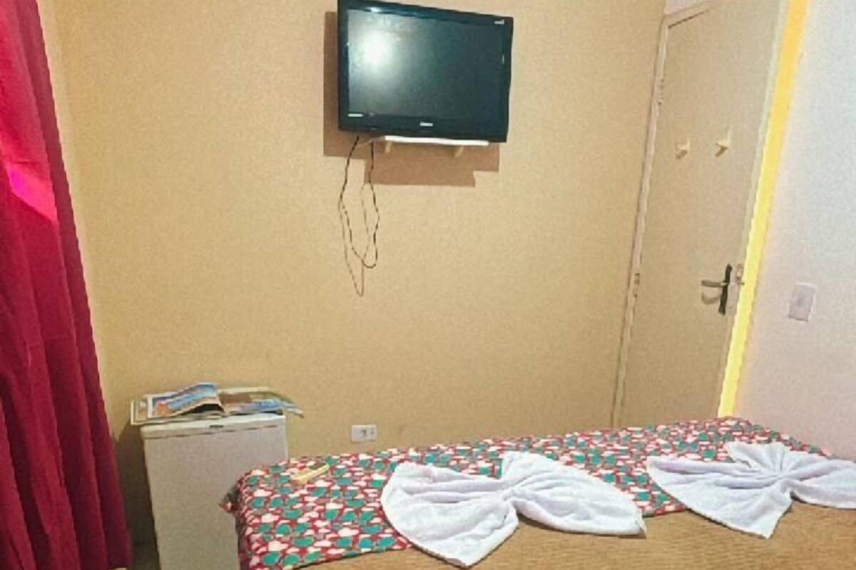 Une chambre d’hôtel avec un lit, un téléviseur fixé au mur, un petit réfrigérateur et une porte dotée d’un éclairage.