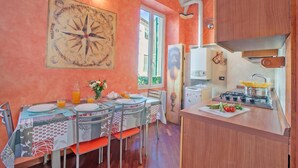 A dining area with a table set for two, a kitchen with a stove, and a large compass wall decoration. - La Perla, Walk to Casino & Old Town, Sanremo, Italy (Sanremo)