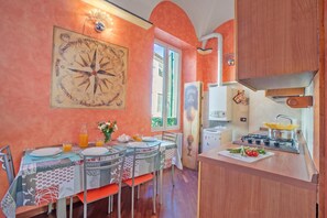A dining area with a table set for two, a kitchen with a stove and pots, and a large compass wall decoration. - La Perla, Walk to Casino & Old Town, Sanremo, Italy (Sanremo)
