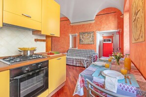 A kitchen with yellow cabinets, a stove, and a dining area with a table set for breakfast. - La Perla, Walk to Casino & Old Town, Sanremo, Italy (Sanremo)
