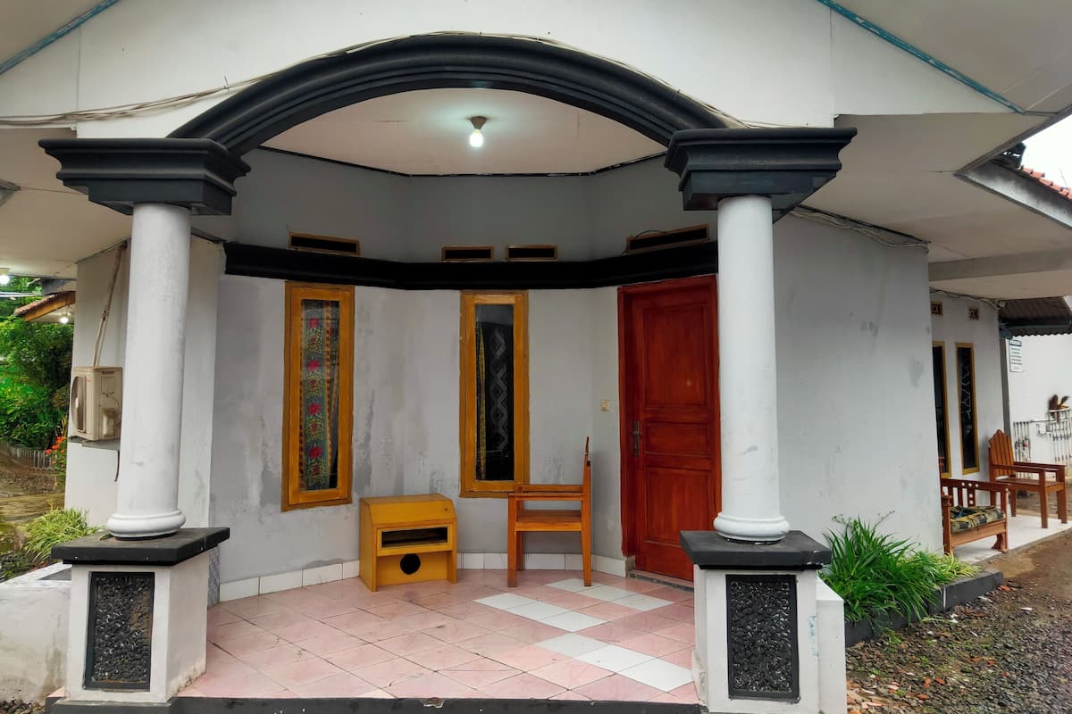 A covered porch with a tiled floor, a wooden bench, a red door, and a small wooden cabinet.