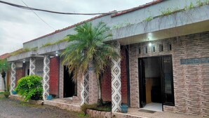 A building with a tiled roof, patterned columns, and a palm tree. - Hotel Intan Niaga (Banjaran)