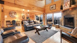 A cozy log cabin interior with a fireplace, leather sofas, and a large wall clock. - Mt Lodge | Sunday River Views | Hot Tub | Game Room (Newry)