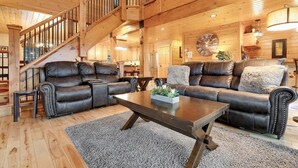 A wooden interior with a staircase, leather sofas, a coffee table, and a clock on the wall. - Mt Lodge | Sunday River Views | Hot Tub | Game Room (Newry)