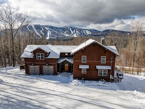 A two-story wooden cabin with a garage, a front porch, and a driveway.