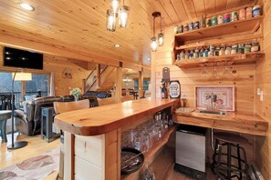A wooden interior with a bar area, shelves with jars, a television, and a staircase.