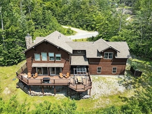 A two-story wooden house with a deck, large windows, and a stone chimney.