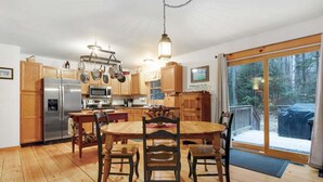 Een keuken met houten kastjes, een roestvrijstalen koelkast, een magnetron en een eettafel met stoelen.