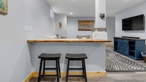 Een bar met twee krukken, een houten toonbank, een wandtelevisie en een decoratief kunstwerk.