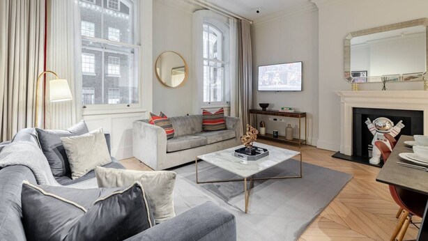Una sala de estar con un sofá gris, una mesa de centro, un televisor y una chimenea con una estatua.