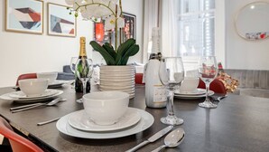 Una mesa de comedor dispuesta con platos, fuentes y cubiertos blancos, una botella de champán y un florero con flores blancas.
