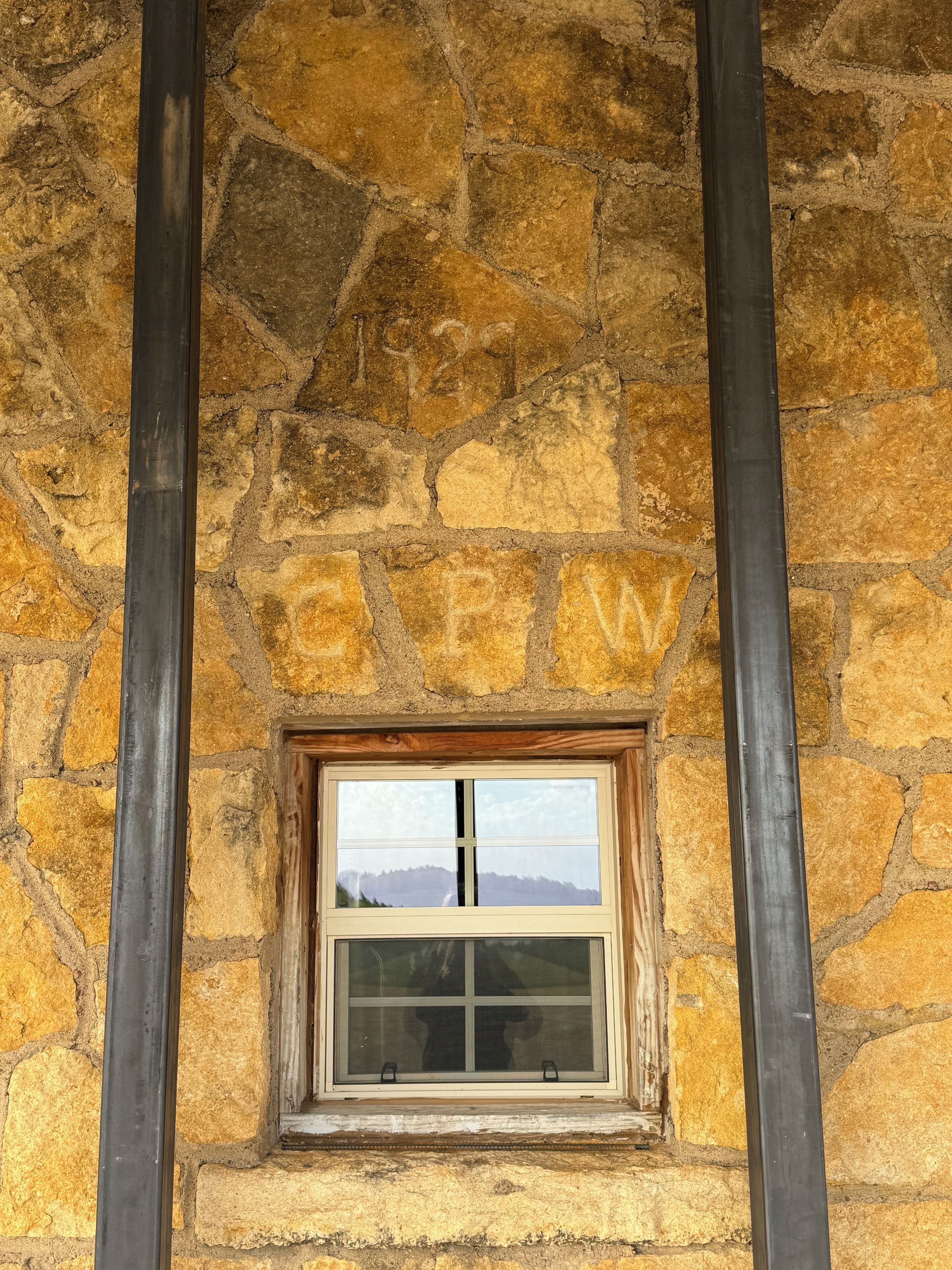 Eine Steinsäule mit einem Holzelement und Fenster, begleitet von zwei vertikalen Metallstreben.