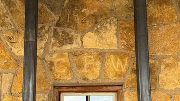 Eine Steinsäule mit einem Holzelement und Fenster, begleitet von zwei vertikalen Metallstreben.