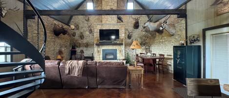 A spacious living room with a stone fireplace, mounted animal heads, and a large TV.