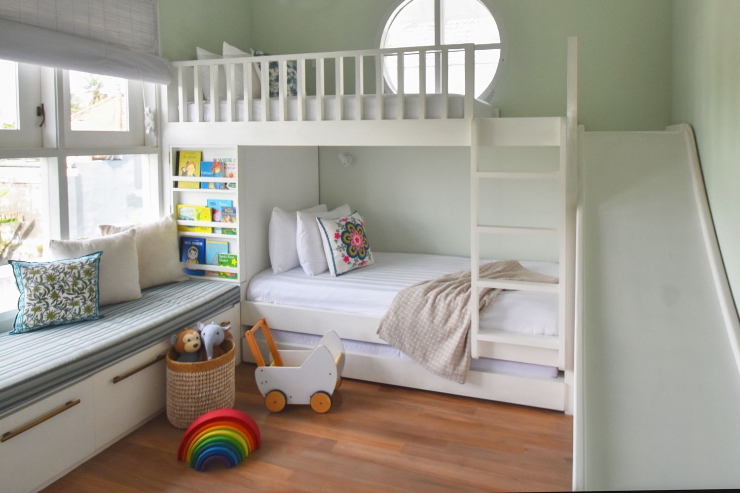 Une chambre d’enfant avec des lits superposés, une bibliothèque, un chariot à jouets et un arc-en-ciel en jouet.