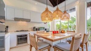 Una cocina moderna con armarios blancos, una isla central con asientos y lámparas colgantes de mimbre.