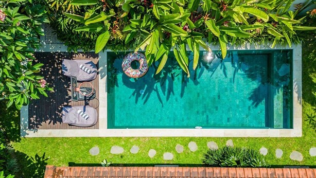Vista aérea de una piscina rodeada de vegetación exuberante, con una zona de terraza que incluye una silla y una toalla.