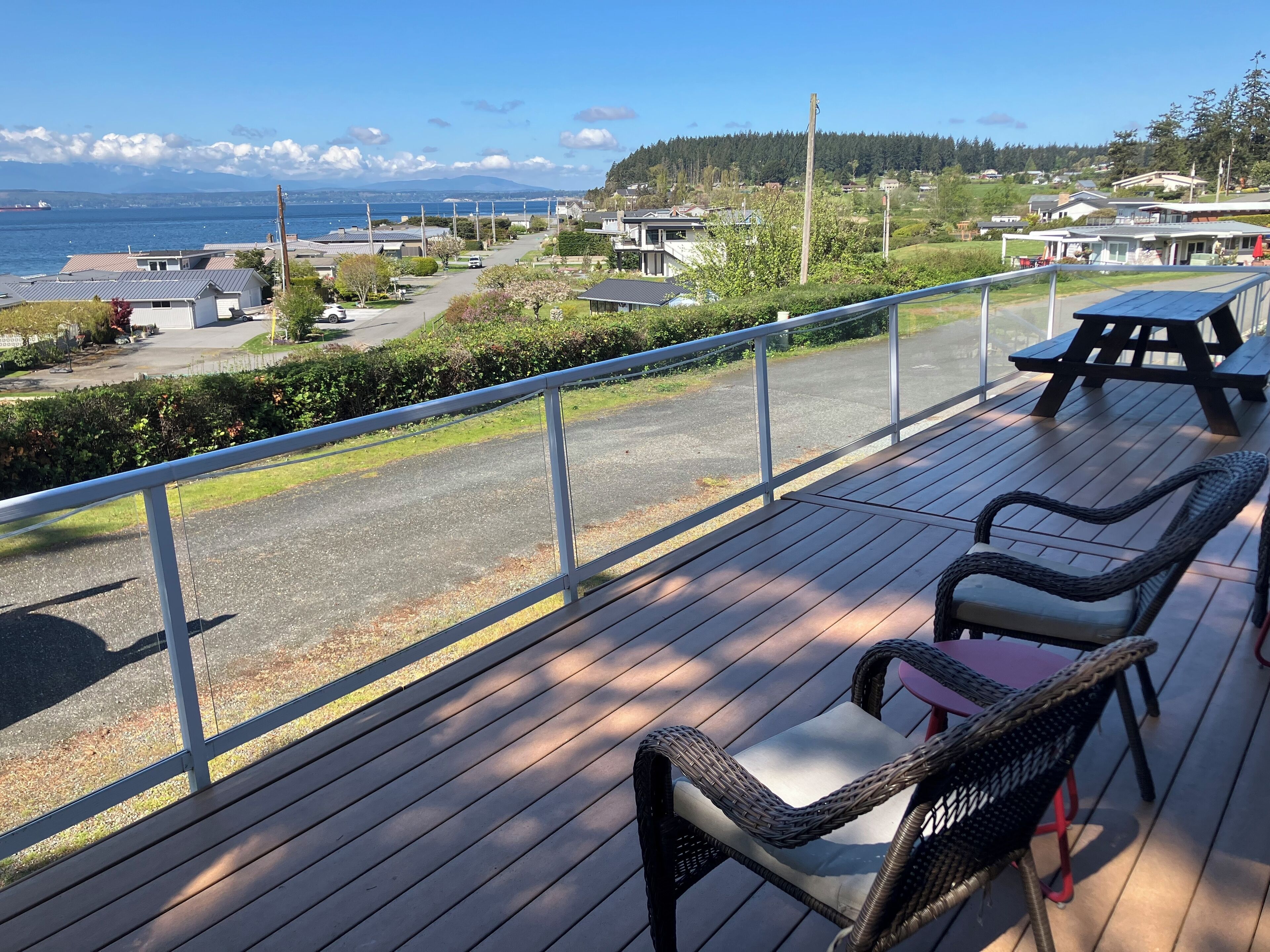 A deck with wicker chairs and a table, overlooking a residential area and a body of water.