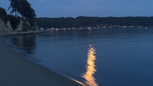 A calm beach at dusk with a visible moon reflection on the water.