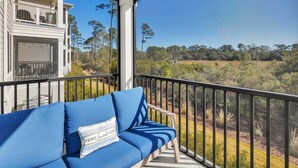 A balcony with a blue sofa and a view of a natural landscape. - Beautifully furnished condo on Jekyll Riverfront! (Jekyll Island)