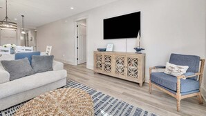 A modern living room with a sofa, a chair, a wooden cabinet, and a flat-screen TV mounted on the wall. - Beautifully furnished condo on Jekyll Riverfront! (Jekyll Island)