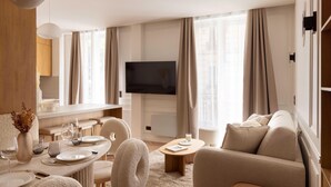 A modern living room with a flat-screen TV, a dining area with a table set for four, and a sofa.