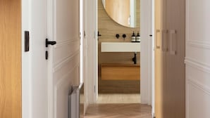 A hallway leading to a bathroom with a wooden floor, white walls, and a large mirror above the sink.